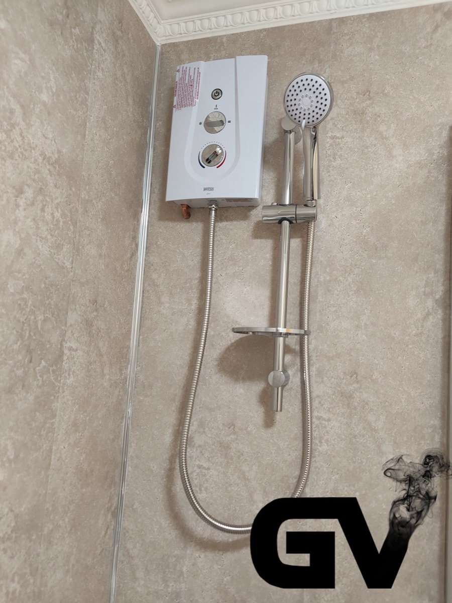 A white electric shower unit and chrome riser rail freshly installed in a tiled shower enclosure.