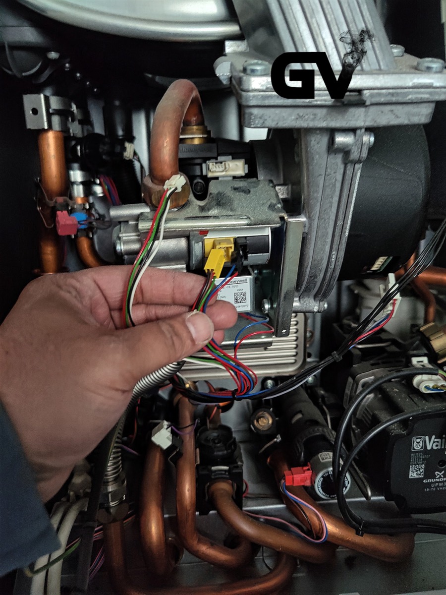 A close-up of a boiler's internal wiring and control board being checked by hand during a repair.